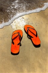 Naklejka premium Orange flip-flops on a sandy beach shoreline.