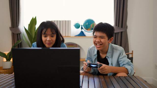 Asian teenage boy and girl playing video games at home together. Concept of digital lifestyle, esports, fun learning, teamwork, and modern entertainment for kids and teens indoors.