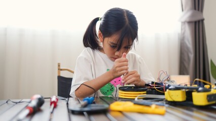 Asian girl assembling robot parts at home, learning STEM and electronics. Developing engineering skills, logical thinking, and problem-solving through hands-on coding education for kids.