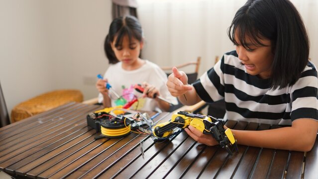 Two Asian girls working together on robotics project at home. Promoting STEM education, teamwork, coding, and problem-solving through hands-on engineering and creative learning.