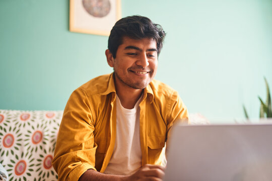 Hombre joven latino reacciona con alegr&iacute;a durante videollamada desde casa. Expresa emoci&oacute;n y conexi&oacute;n humana en contexto de teletrabajo. Perfecta para representar logros o buenas noticias laborales.

