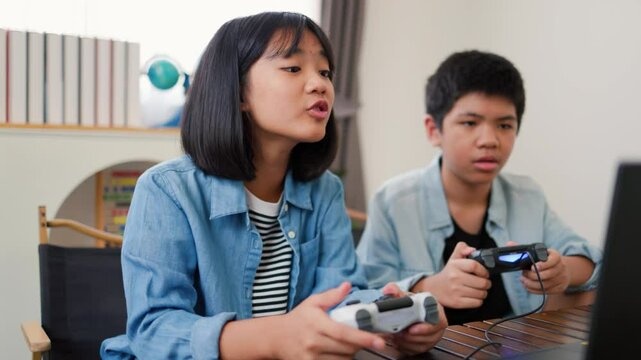 Asian teenage boy and girl playing video games at home together. Concept of digital lifestyle, esports, fun learning, teamwork, and modern entertainment for kids and teens indoors.