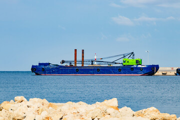 A vibrant blue ship, equipped with cranes and various tools, is anchored close to the rocky...