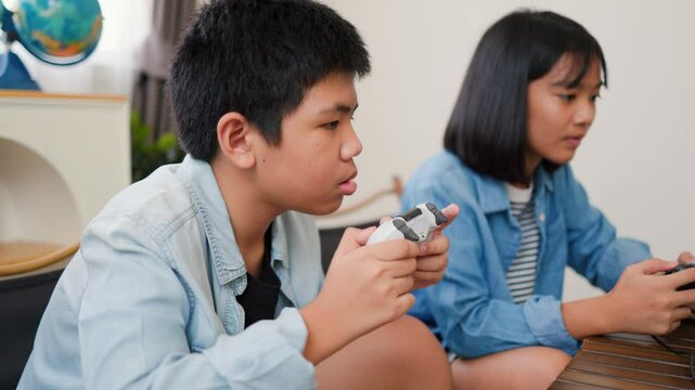 Asian teenage boy and girl playing video games at home together. Concept of digital lifestyle, esports, fun learning, teamwork, and modern entertainment for kids and teens indoors.