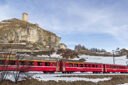 Ardez, Switzerland - January 27.2022: Ruins Steinsberg from the ancient Medieval Castle Steinsberg with a running red passenger train from the  Rhatian railway company.