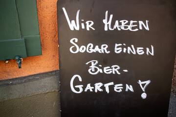 Tafel mit der handschriftlichen Aufschrift "Wir haben sogar einen Biergarten" vor einer Gaststätte