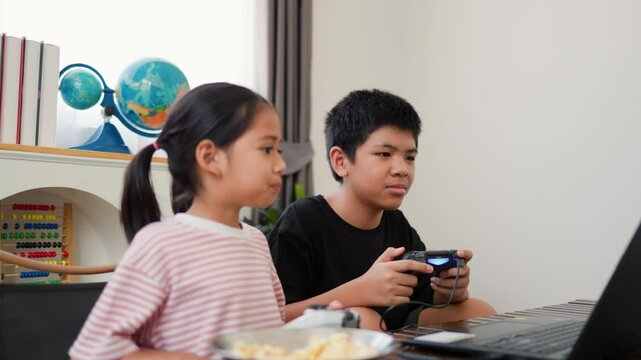 Asian teenage boy and girl playing video games at home together. Concept of digital lifestyle, esports, fun learning, teamwork, and modern entertainment for kids and teens indoors.