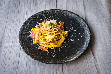 Carbonara with ham cream and cheese served on a black plate
