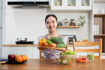 Fit woman enjoys healthy fresh vegetables and fruits breakfast sitting in the kitchen.