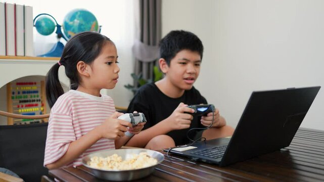 Asian teenage boy and girl playing video games at home together. Concept of digital lifestyle, esports, fun learning, teamwork, and modern entertainment for kids and teens indoors.