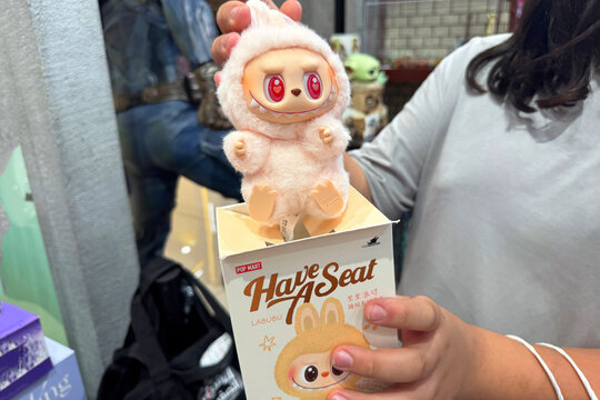 Dubai, UAE - May 18, 2025: Close-up of Pop Mart Labubu Have A Seat plush figure with red eyes held by customer in store. Trending collectible toy from The Monsters series, popular on TikTok and reels