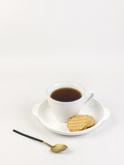 Minimalist flat lay of a white cup filled with black tea served with two butter cookies on a white plate, placed on a clean white background.