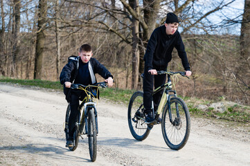 Obraz premium Two boys enjoy a bike ride on a dirt road through the woods on a sunny day.