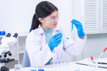Young girl in goggles analyzing blue liquid sample in test tube during science experiment. Science,...