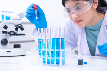 Teen scientist girl conducting science test by carefully evaluating blue solution in laboratory....