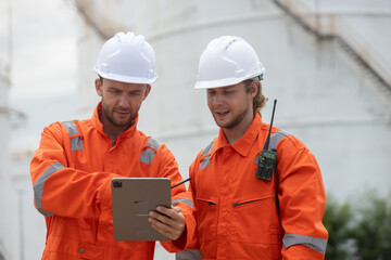 Worker in safety gear using tablet near industrial storage oil tanks refining petrochemical...