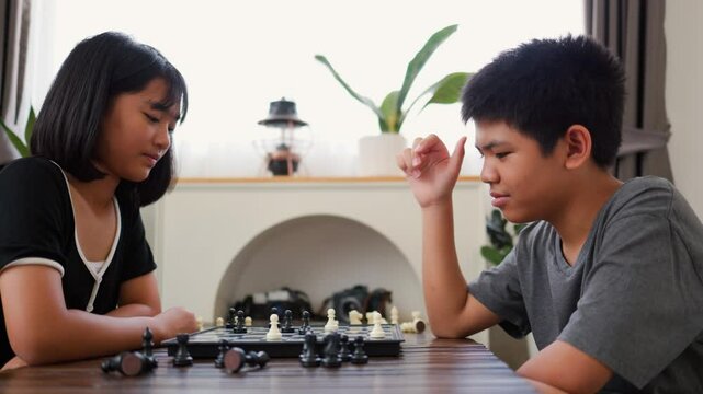 Asian teenage boy and girl playing chess at home, developing strategic thinking, logic, and concentration. Concept of brain training, youth education, and indoor board game activity.