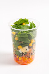A colorful salad cup featuring fresh spinach, corn, and diced vegetables stacked beautifully