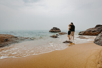 Couple embracing on rocky beach with gentle waves and overcast sky