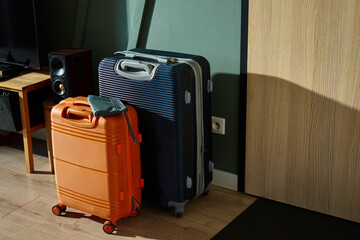 Two modern suitcases, orange and navy, stand near entrance door in morning light. Packed luggage in...