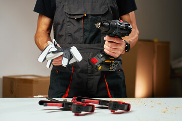 Person in work overalls holding cordless power drill and safety gloves at workbench with tools and...
