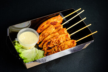 Skewered chicken satay is beautifully arranged with a side of creamy sauce and crisp lettuce