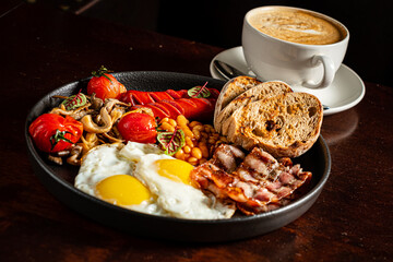 A hearty breakfast of fried eggs, crispy bacon, tomatoes, mushrooms, and coffee