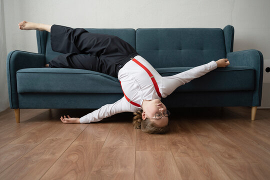 Teenage girl lying upside down on a couch in a living room wearing glasses and red suspenders