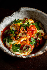 A flavorful dish featuring eggs in a rich tomato sauce, garnished with fresh herbs and greens