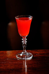 A striking red drink in an elegant glass stands alone on a rich wooden surface, inviting curiosity