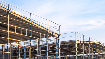 Metal structure of 2 factory warehouse industry buildings in construction site against pale blue sky background, low angle and perspective side view