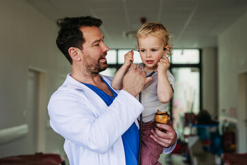 Handsome doctor holding young pediatric patient in arms.