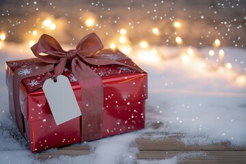 Elegant Christmas gift box wrapped in glossy red paper with a silky ribbon and a blank tag, placed on a snow-dusted wooden surface with soft glowing fairy lights in the background. 