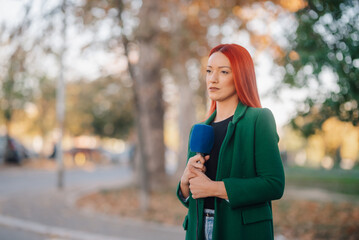 Serious female journalist reporting live news holding microphone