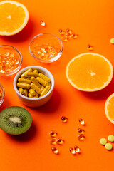 Many vitamins and minerals, dietary supplements in small glass bowls, orange, kiwi, lime and lemon as sources of natural vitamins and minerals. Vitamins and fruits from above on a blue background