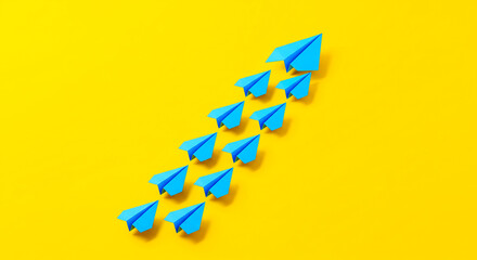 Fototapeta premium A group of blue paper airplanes flying upwards on a bright yellow background in a diagonal arrangement