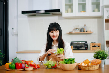 Asian woman preparing healthy food with smartphone in home kitchen. Great for wellness, clean eating, cooking content