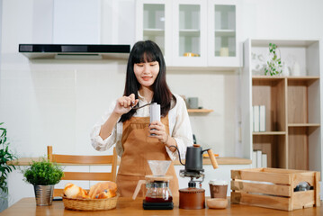 Asian woman barista brewing coffee with kettle and smiling in cozy cafe kitchen. Great for themes of cafe, startup, coffee