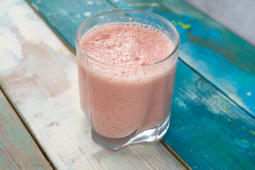 Fresh pink smoothie in clear glass on colorful wood background. Healthy refreshing drink for wellness and nutrition concept. Natural and organic beverage.