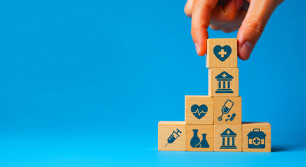 Hand placing wooden block with heart symbol on top of stack of medical icons on blue background
