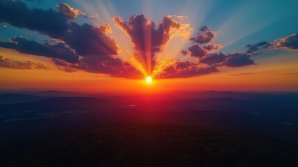 Obraz premium Vibrant sunset with radiant sunbeams over rolling hills and silhouetted horizon