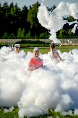 Children playing in outdoor foam party with bubbles on a sunny day