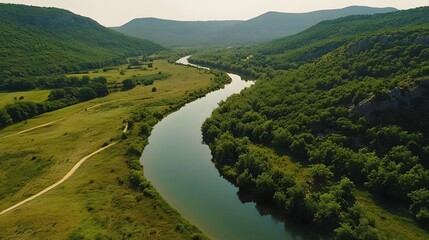 Aerial photograph showcases a meandering river within a lush, green valley bordered by steep cliffs and dense forest.