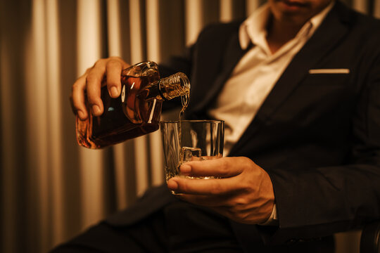 A stylish man holds a glass of whiskey at an upscale bar, enjoying a luxurious indoor celebration with friends and fine alcohol.