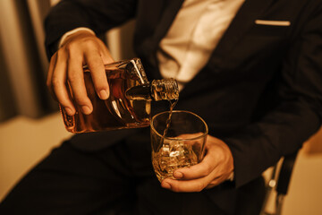 A stylish man holds a glass of whiskey at an upscale bar, enjoying a luxurious indoor celebration with friends and fine alcohol.