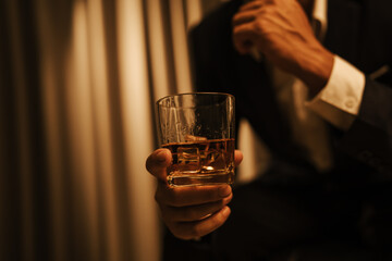 A stylish man holds a glass of whiskey at an upscale bar, enjoying a luxurious indoor celebration with friends and fine alcohol.