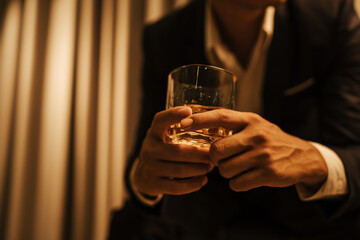 A stylish man holds a glass of whiskey at an upscale bar, enjoying a luxurious indoor celebration with friends and fine alcohol.