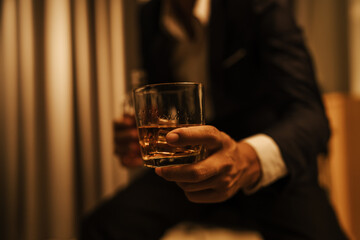 A stylish man holds a glass of whiskey at an upscale bar, enjoying a luxurious indoor celebration with friends and fine alcohol.