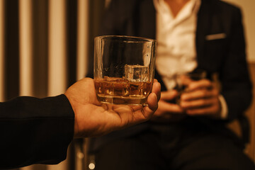A stylish man holds a glass of whiskey at an upscale bar, enjoying a luxurious indoor celebration with friends and fine alcohol.