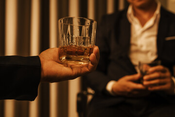 A stylish man holds a glass of whiskey at an upscale bar, enjoying a luxurious indoor celebration with friends and fine alcohol.